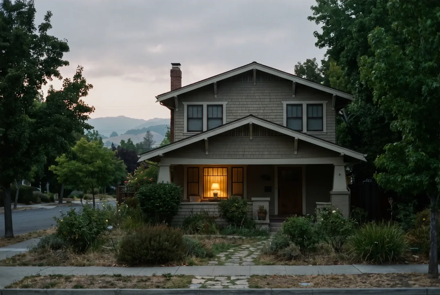 A brick bungalow in an old Reno neighborhood at dusk, porch light on